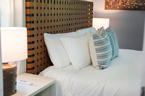 Woven leather headboard with white bedding and striped pillows.