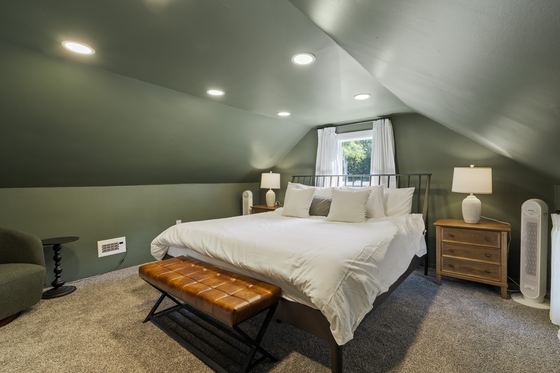 Upstairs bedroom with a king bed, green walls, sloped ceiling and a leather bench.