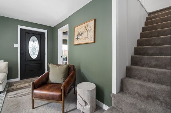 Entry with sage green walls, a leather armchair, and stairs to the upper floor.