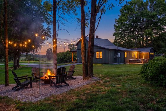 Fire pit ringed with Adirondack chairs under string lights at dusk.