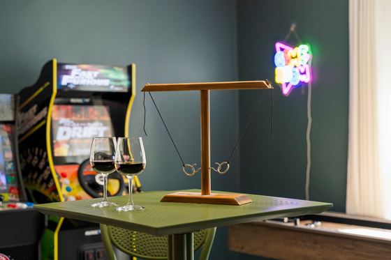 High-top table with wine glasses, arcade cabinet and neon sign behind.