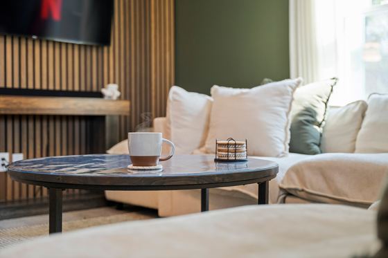 Round side table with a coffee cup, sectional and slatted wall behind.