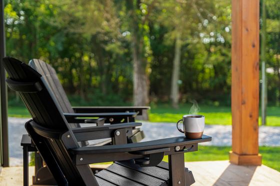 A mug of coffee resting on the arm of a porch chair in morning light.